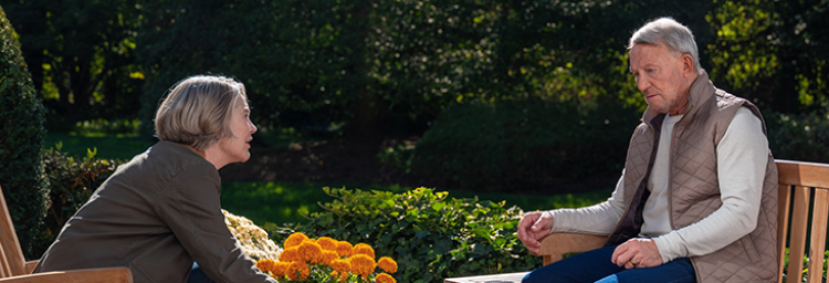 An elderly couple chatting while sitting outside on the patio. Actor portrayal